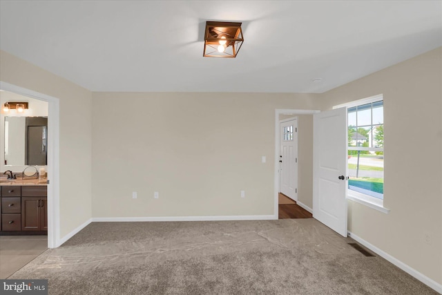 unfurnished bedroom featuring visible vents, light colored carpet, ensuite bath, and baseboards