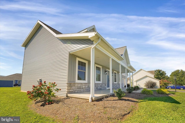 view of side of property featuring stone siding, covered porch, a lawn, and roof with shingles