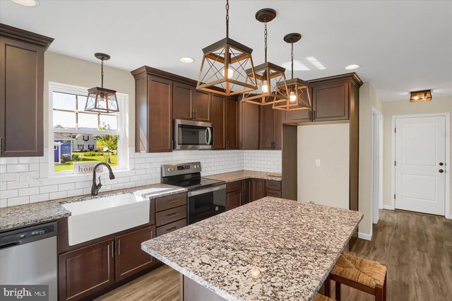 kitchen with light wood-style flooring, a sink, light stone counters, appliances with stainless steel finishes, and an inviting chandelier