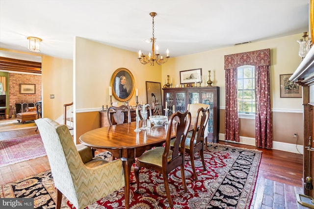 dining area featuring an inviting chandelier, dark hardwood / wood-style flooring, and a brick fireplace