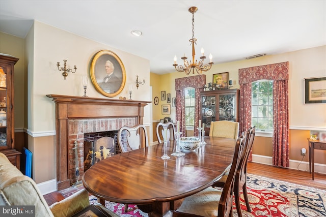 dining area featuring a notable chandelier, wood-type flooring, and a brick fireplace