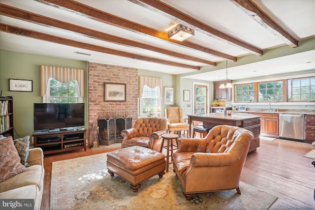 living room with light hardwood / wood-style floors, a brick fireplace, beamed ceiling, sink, and a chandelier