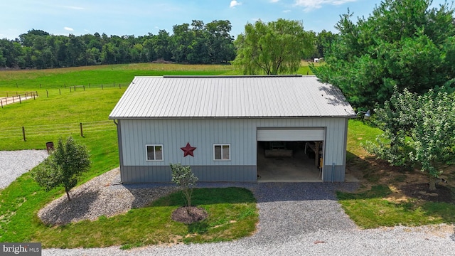 view of outdoor structure with an outbuilding, gravel driveway, a rural view, and fence