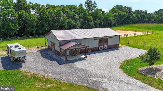 view of front facade featuring gravel driveway, an exterior structure, metal roof, a rural view, and an outdoor structure