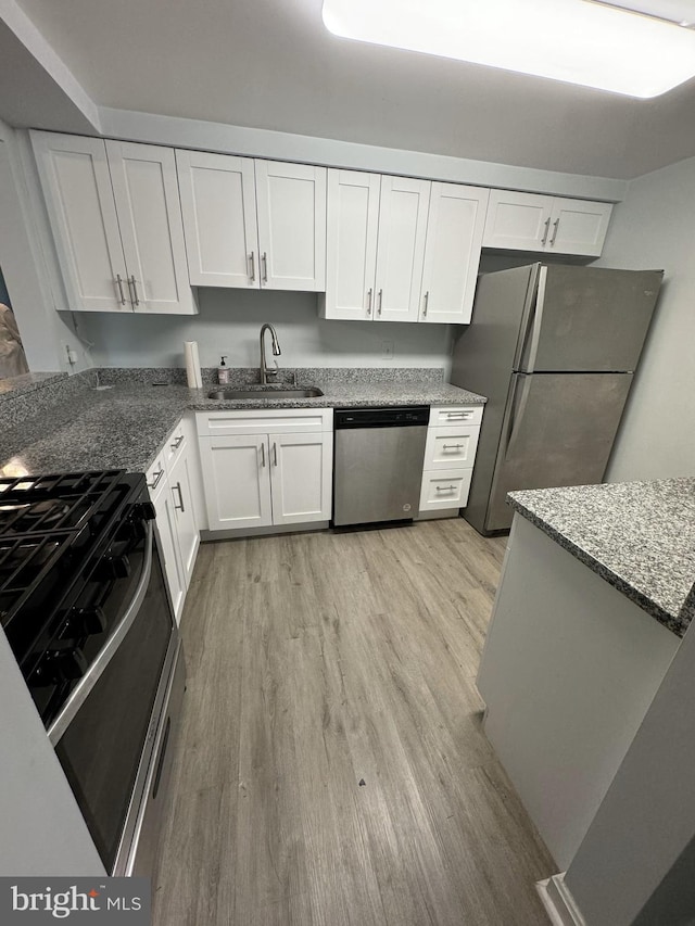 kitchen with white cabinetry, stainless steel appliances, light wood-type flooring, dark stone counters, and sink