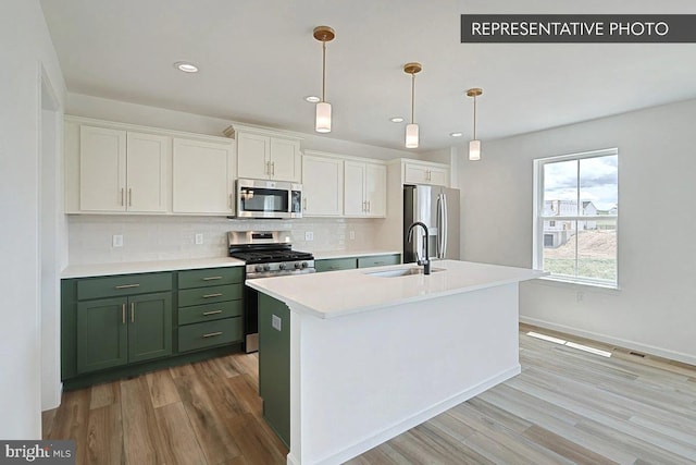 kitchen with a kitchen island with sink, stainless steel appliances, sink, light wood-type flooring, and white cabinets