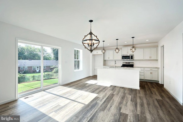 kitchen with appliances with stainless steel finishes, white cabinetry, dark hardwood / wood-style floors, pendant lighting, and a center island with sink