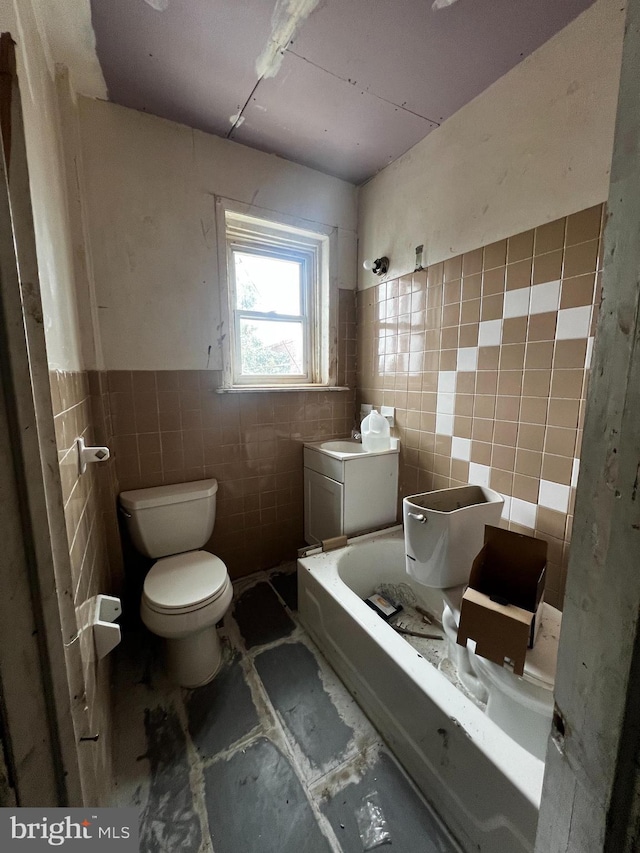 bathroom with tile walls, a bathtub, and toilet