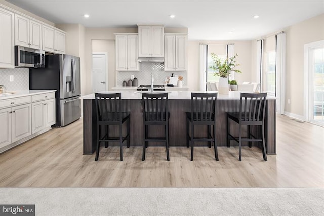 kitchen featuring a kitchen island with sink, a healthy amount of sunlight, stainless steel appliances, and white cabinets