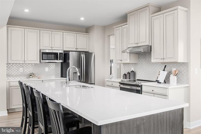 kitchen featuring an island with sink, light hardwood / wood-style floors, stainless steel appliances, and a breakfast bar area