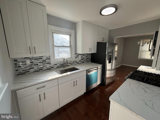 kitchen with light stone counters, white cabinetry, stainless steel appliances, and a sink