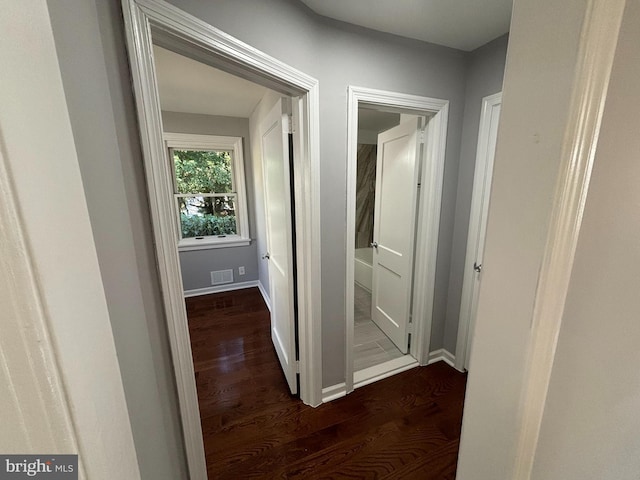 hall with visible vents, baseboards, and dark wood finished floors