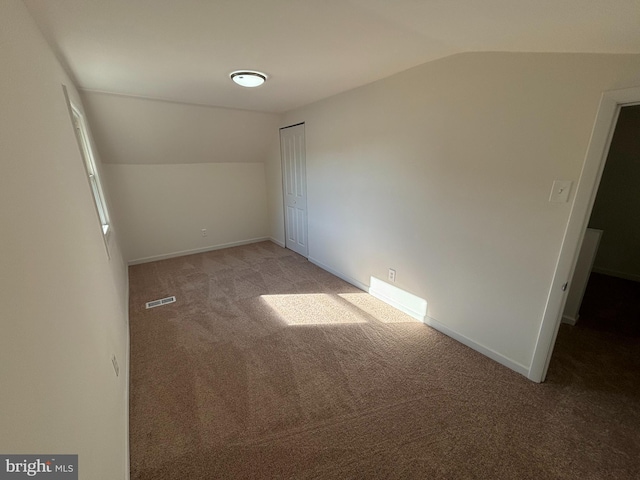 spare room featuring visible vents, light colored carpet, baseboards, and lofted ceiling