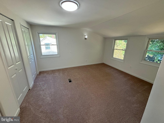 unfurnished room with baseboards, lofted ceiling, visible vents, and dark carpet