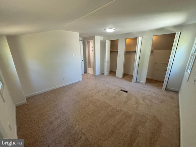 unfurnished bedroom featuring visible vents, baseboards, multiple closets, and light carpet