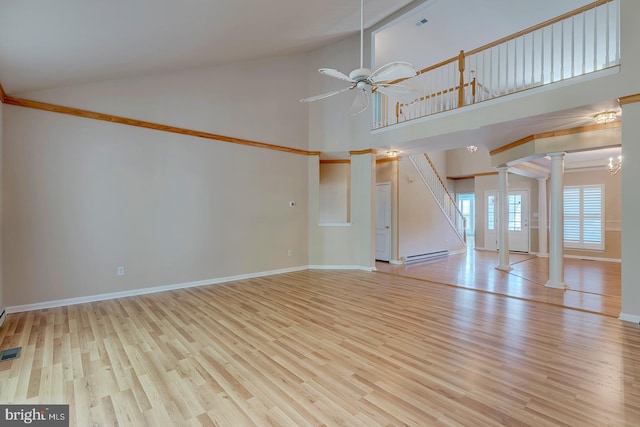 unfurnished living room with ceiling fan, baseboard heating, high vaulted ceiling, light wood-type flooring, and ornate columns