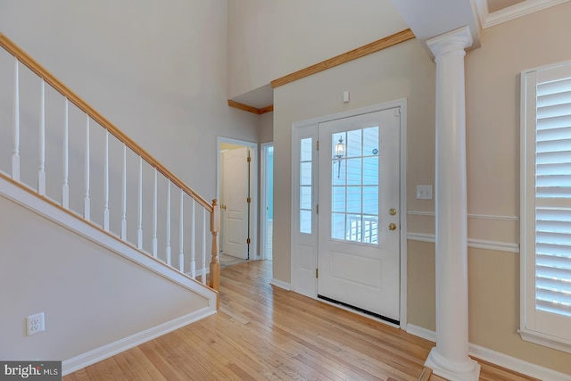 entryway featuring crown molding, decorative columns, light hardwood / wood-style flooring, and a high ceiling