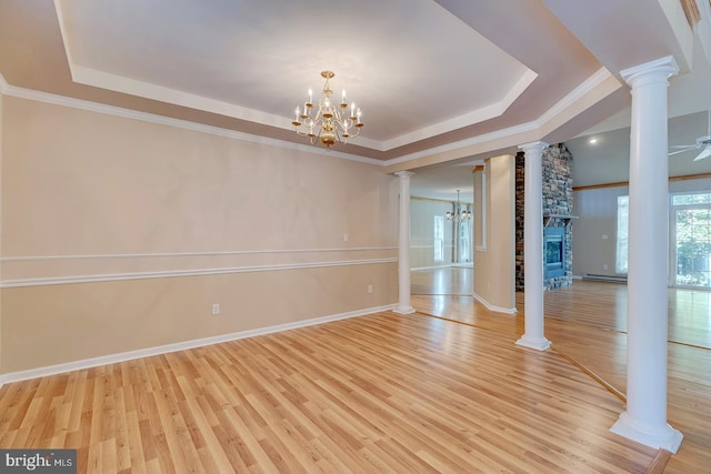 spare room featuring a stone fireplace, light hardwood / wood-style floors, ceiling fan with notable chandelier, crown molding, and a tray ceiling