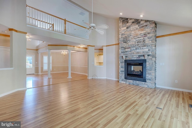 unfurnished living room featuring high vaulted ceiling, ceiling fan, a stone fireplace, light hardwood / wood-style floors, and decorative columns