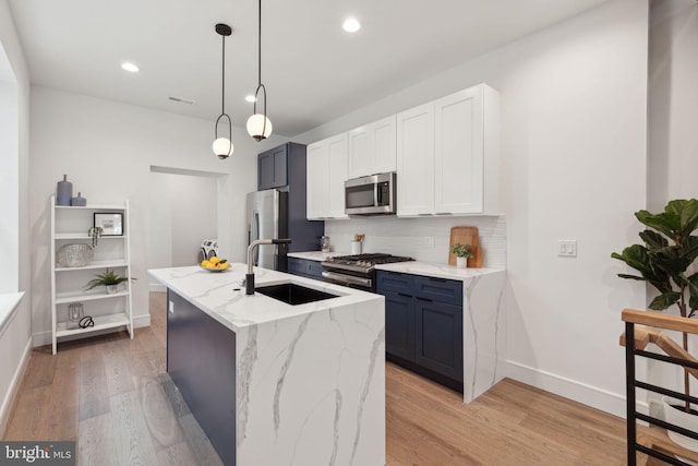 kitchen featuring a kitchen island with sink, white cabinetry, light hardwood / wood-style flooring, appliances with stainless steel finishes, and decorative light fixtures