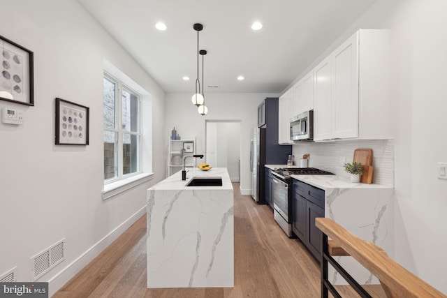 kitchen with hanging light fixtures, stainless steel appliances, light hardwood / wood-style flooring, a kitchen island with sink, and sink