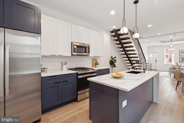 kitchen featuring light hardwood / wood-style floors, white cabinetry, light stone counters, pendant lighting, and stainless steel appliances