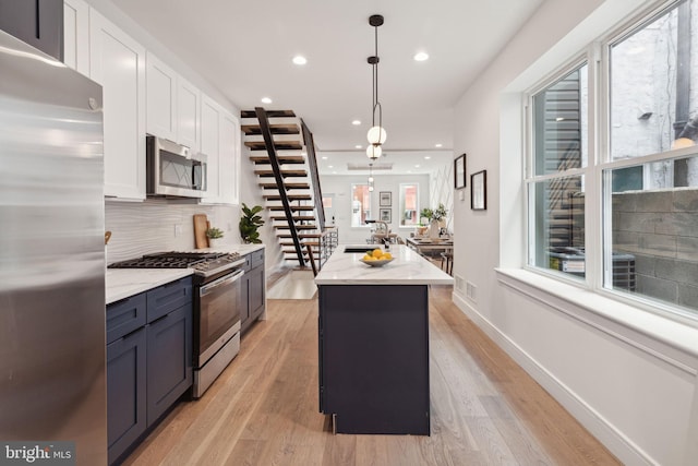 kitchen with white cabinets, a kitchen island, decorative light fixtures, stainless steel appliances, and light wood-type flooring