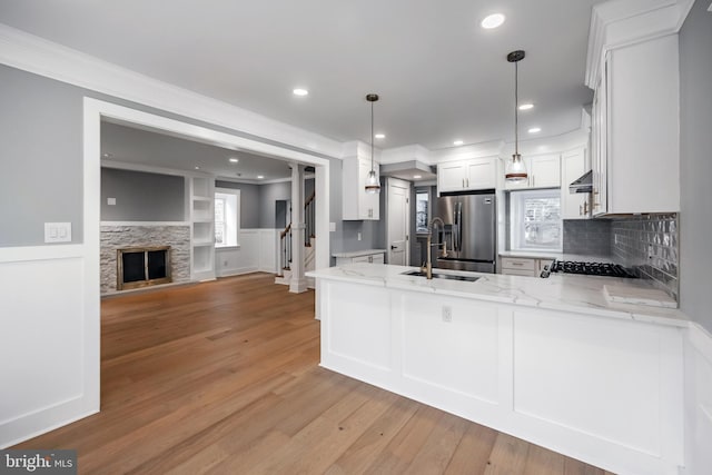 kitchen with white cabinets, kitchen peninsula, hanging light fixtures, light stone countertops, and stainless steel fridge with ice dispenser