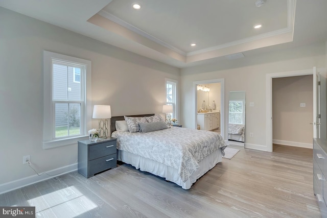 bedroom with light hardwood / wood-style flooring, ensuite bath, and a raised ceiling