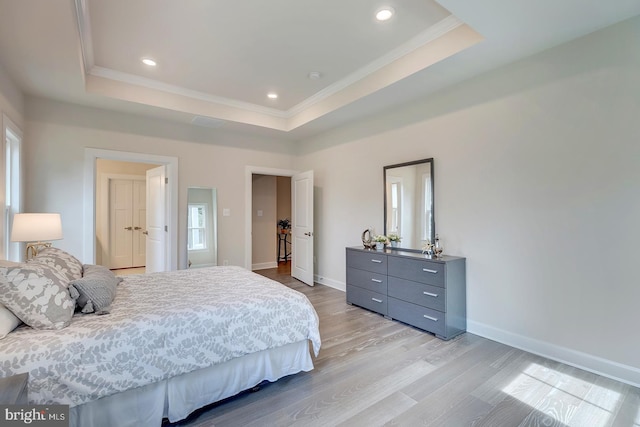 bedroom with ornamental molding, light hardwood / wood-style flooring, and a raised ceiling