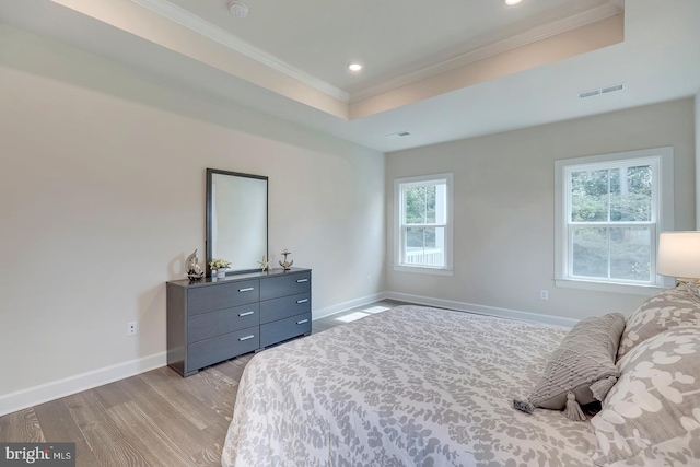 bedroom featuring light wood-type flooring, crown molding, and a raised ceiling