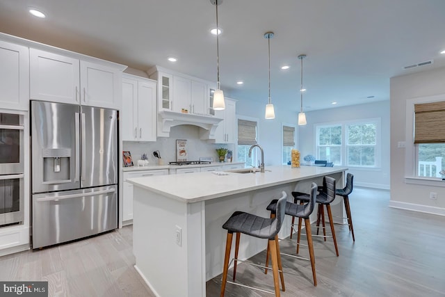 kitchen with sink, an island with sink, white cabinetry, hanging light fixtures, and stainless steel appliances