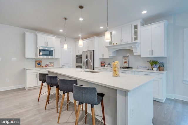 kitchen featuring white cabinetry, a center island with sink, appliances with stainless steel finishes, and hanging light fixtures