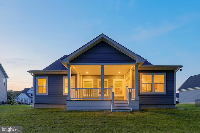 back house at dusk with a yard and a porch