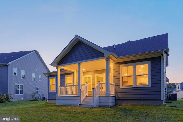 back house at dusk featuring cooling unit, a yard, and covered porch