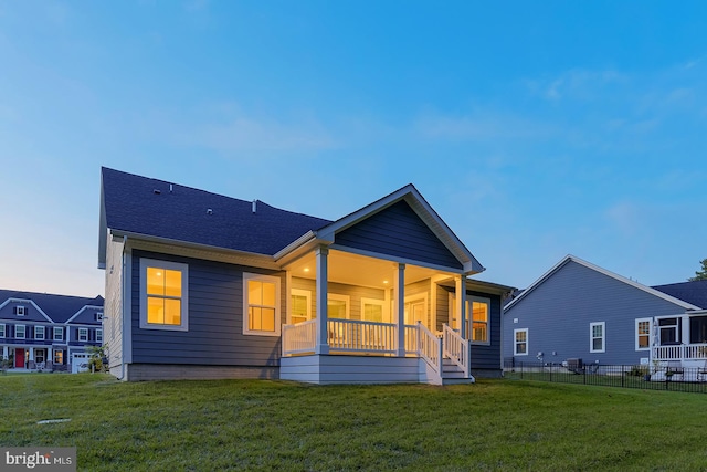 back house at dusk with a porch and a lawn