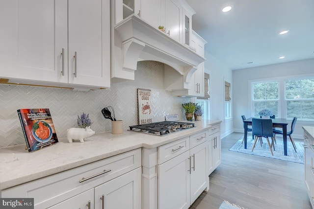 kitchen with decorative backsplash, white cabinetry, light stone counters, light wood-type flooring, and stainless steel gas stovetop