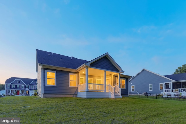 back house at dusk with a porch and a yard