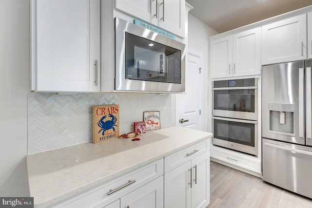 kitchen featuring backsplash, white cabinetry, appliances with stainless steel finishes, light stone countertops, and light hardwood / wood-style floors