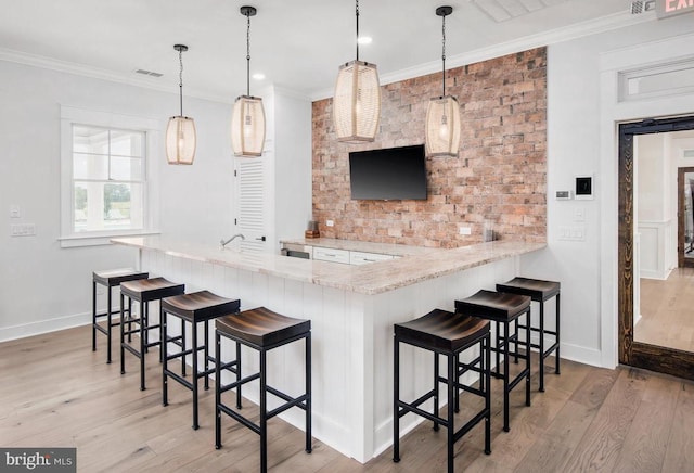 kitchen with light hardwood / wood-style floors, kitchen peninsula, a kitchen bar, decorative light fixtures, and ornamental molding