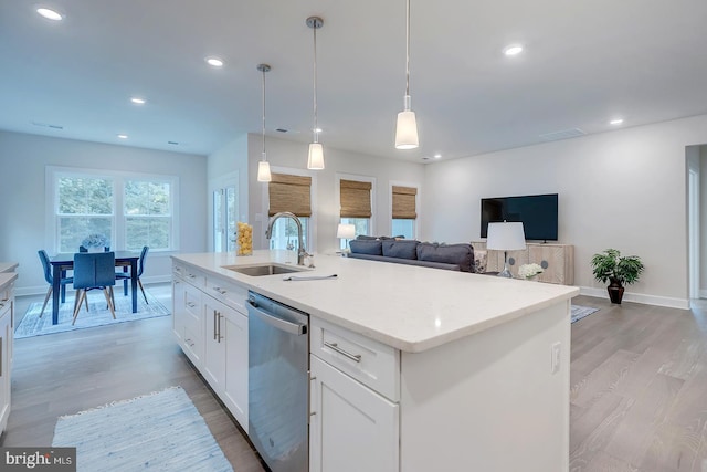 kitchen featuring dishwasher, a kitchen island with sink, sink, white cabinets, and hanging light fixtures