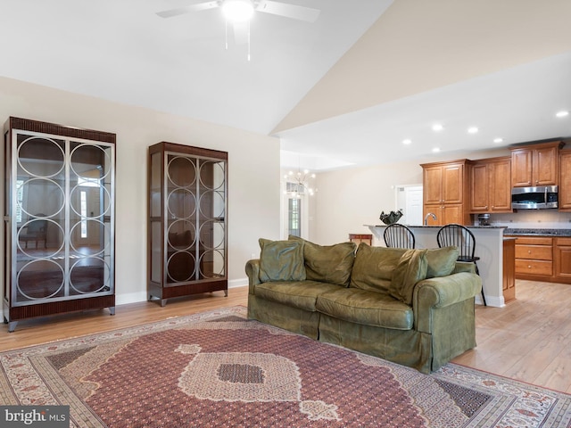 living room with baseboards, recessed lighting, light wood-style flooring, ceiling fan with notable chandelier, and high vaulted ceiling