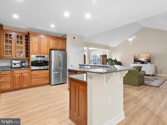 kitchen with open floor plan, brown cabinets, appliances with stainless steel finishes, and a kitchen bar