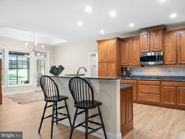 kitchen with a breakfast bar area, light wood-style floors, brown cabinetry, stainless steel appliances, and a kitchen island with sink