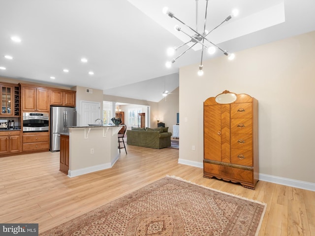 kitchen featuring open floor plan, a breakfast bar area, lofted ceiling, appliances with stainless steel finishes, and brown cabinetry