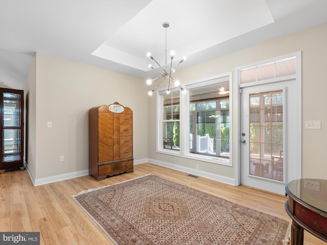 dining area with baseboards, visible vents, light wood finished floors, a raised ceiling, and a notable chandelier