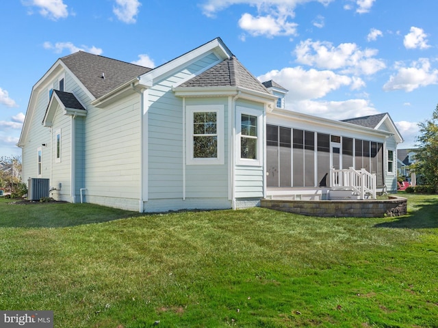 back of house featuring central AC unit, roof with shingles, a yard, and a sunroom