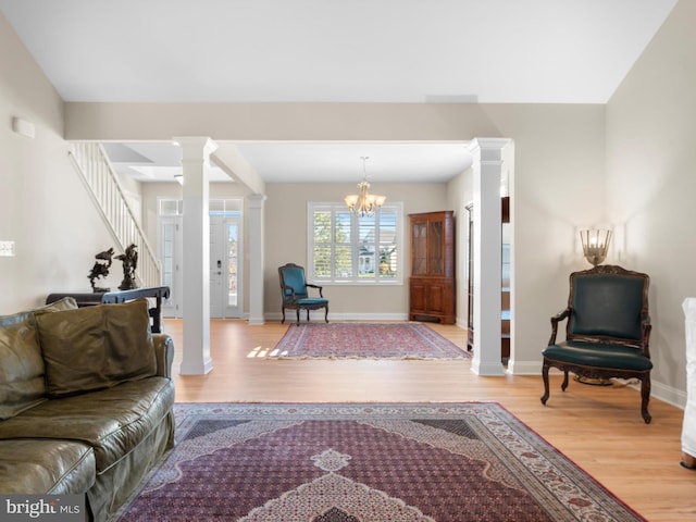 living area featuring stairs, light wood-style floors, baseboards, and ornate columns