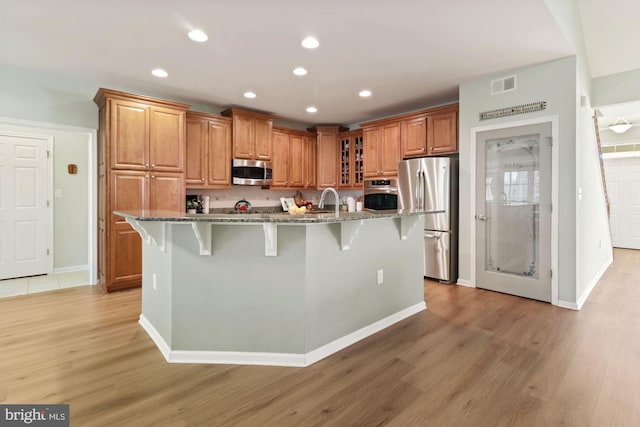 kitchen featuring light wood-type flooring, stainless steel appliances, stone countertops, and a breakfast bar