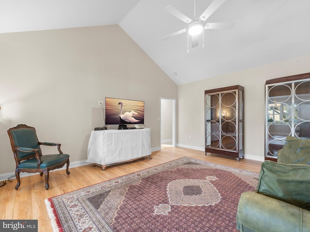 living area with baseboards, high vaulted ceiling, wood finished floors, and a ceiling fan